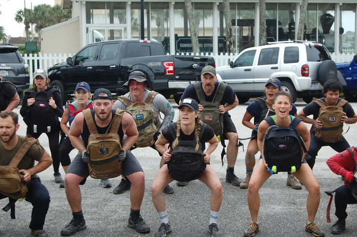 Group of people outdoors doing squats with GORUCK rucksacks during a rucking workout