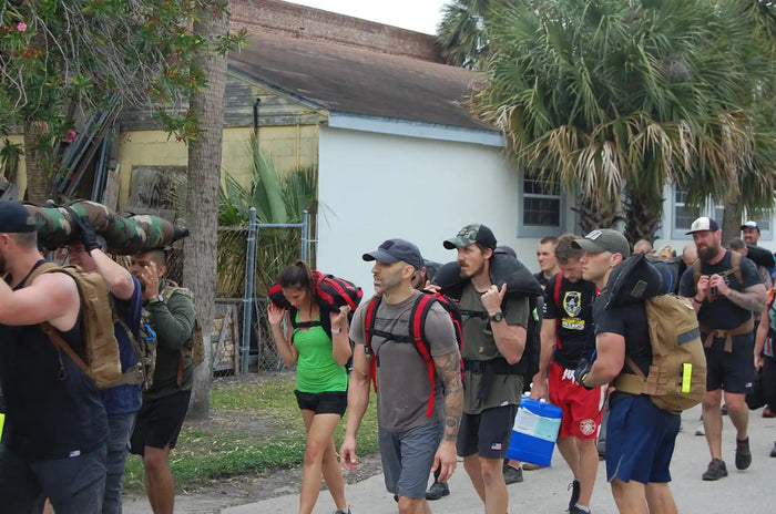 Group of people rucking outdoors with weighted backpacks and sandbags during GORUCK event