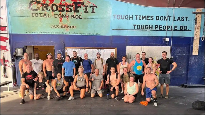 Group of athletes posing inside CrossFit gym under 'Tough times don't last. Tough people do.' mural