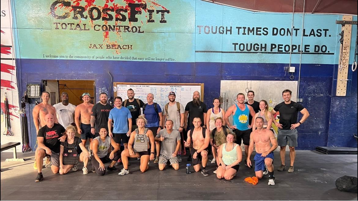 Group of athletes posing in front of CrossFit Total Control gym wall, showcasing fitness community and GORUCK training spirit.