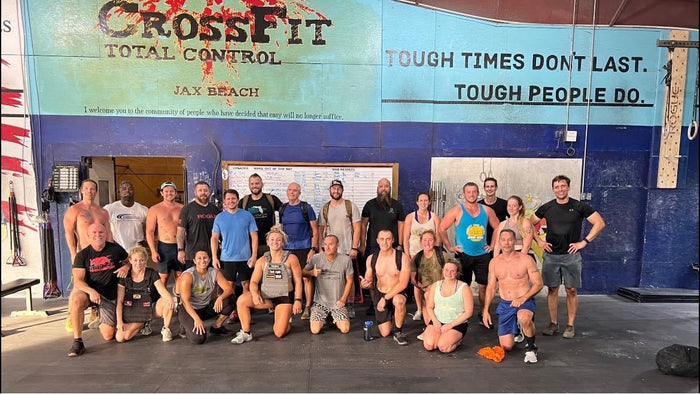 Group of athletes posing in front of CrossFit Total Control gym wall, showcasing fitness community and GORUCK training spirit.