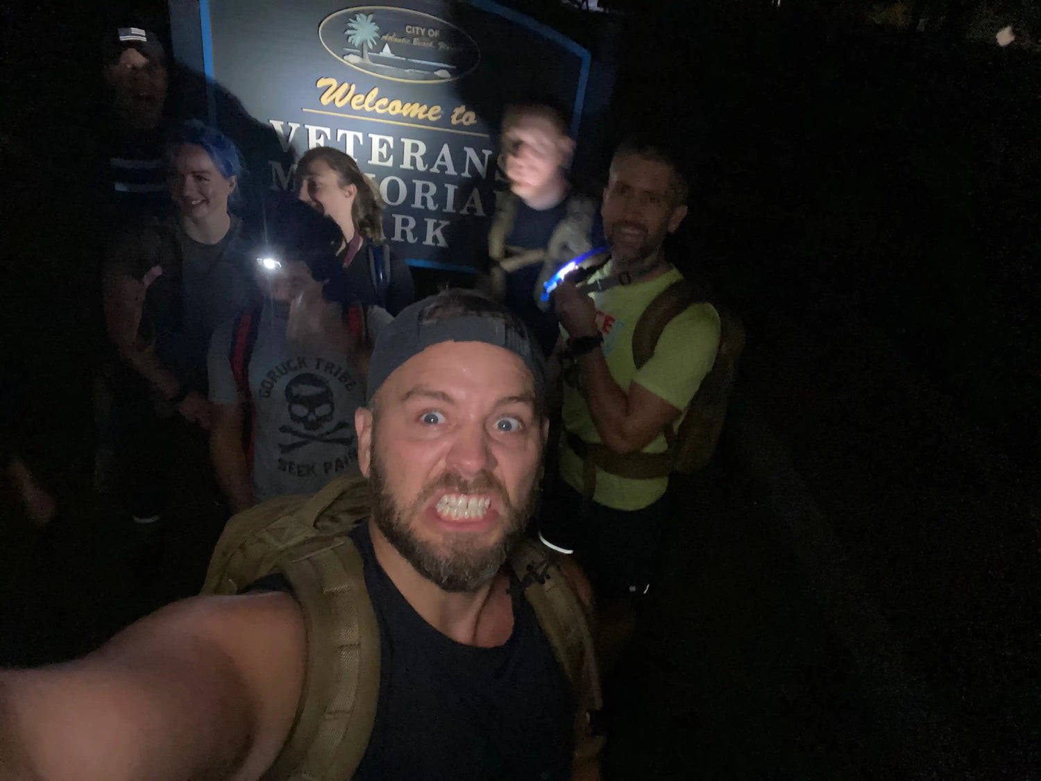 GORUCK team with rucksacks at night in front of Veteran Memorial Park sign