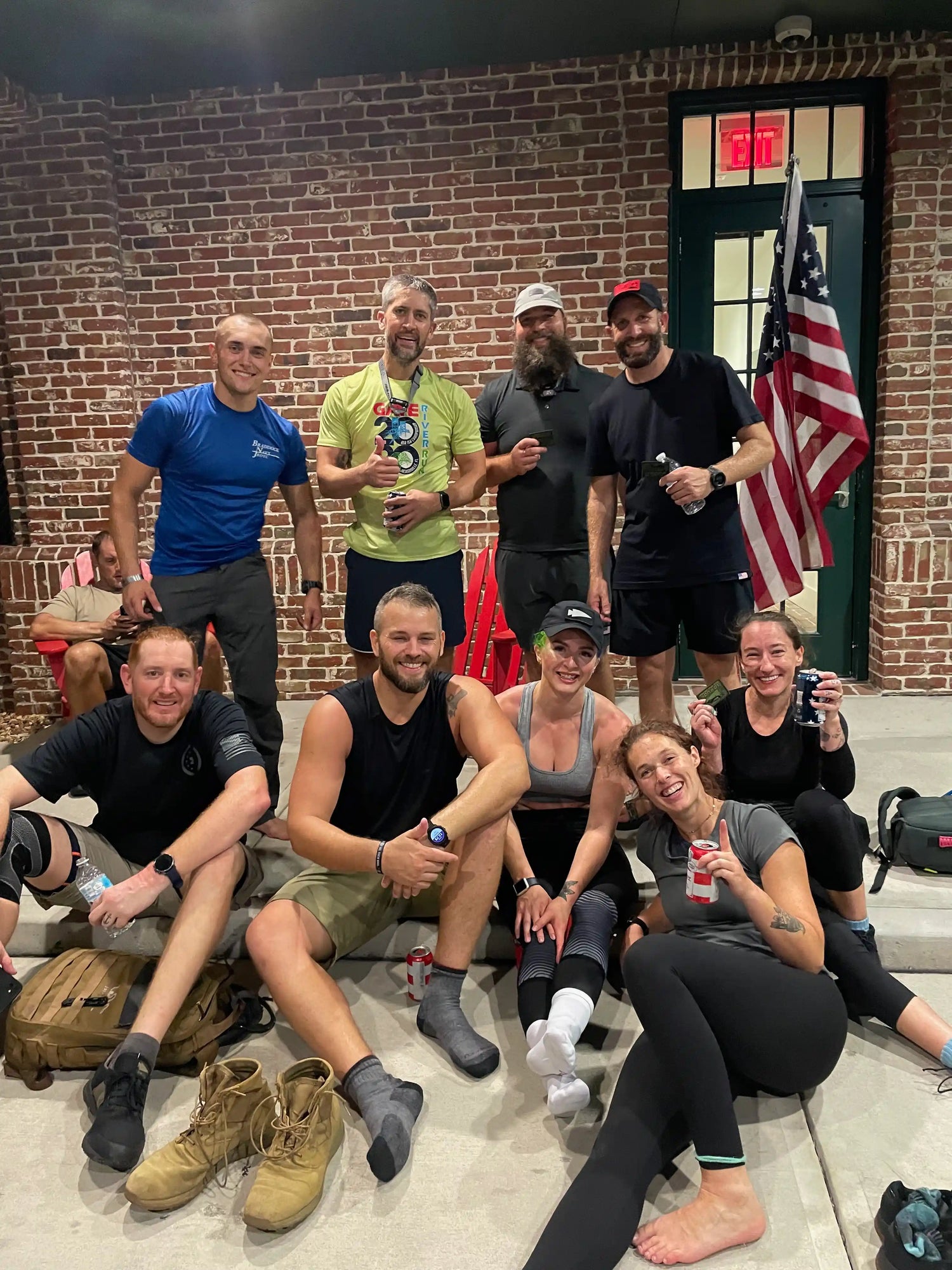 Smiling GORUCK rucking team relaxing indoors, posing with an American flag and gear bags.