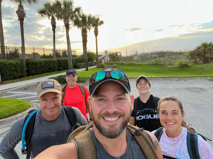 Five people rucking with backpacks outdoors near palm trees at sunrise, goruck.mommunity event