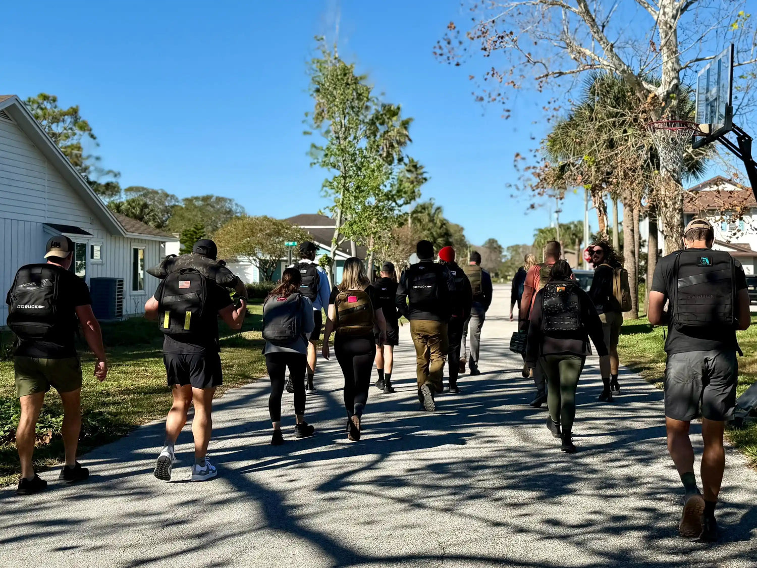 Group of people rucking with GORUCK backpacks outdoors in a sunny suburban neighborhood
