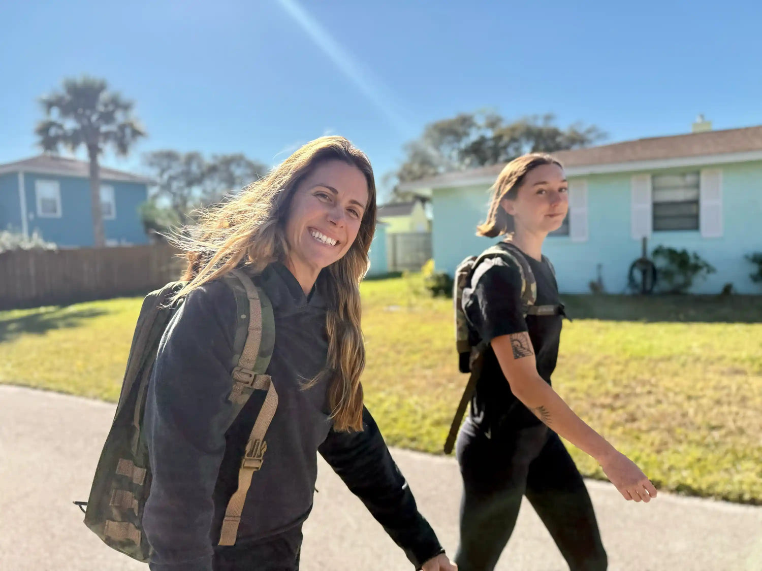 Two women rucking outdoors with GORUCK backpacks on a sunny suburban street