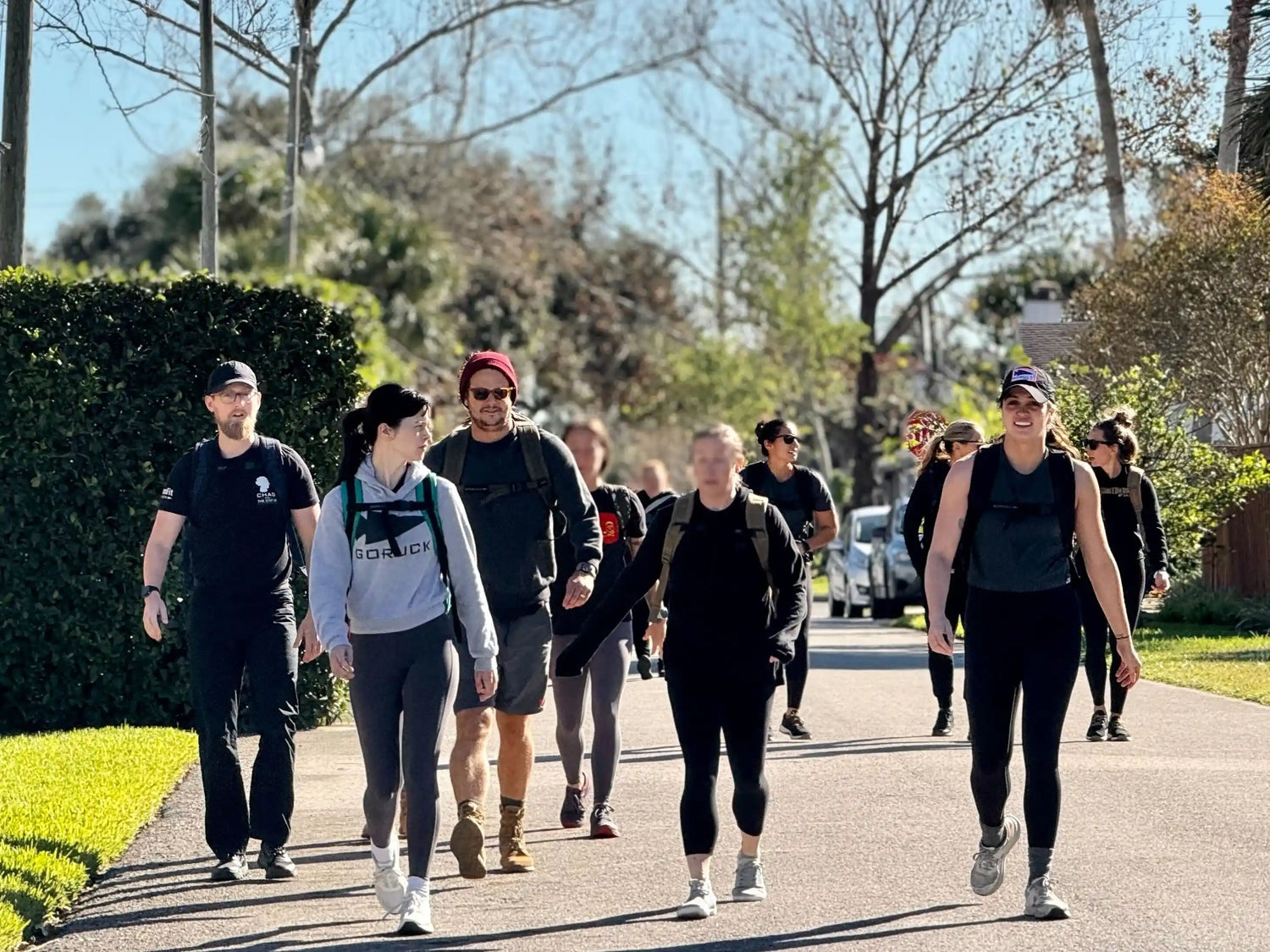 Group of people rucking outdoors wearing GORUCK gear on a sunny neighborhood street