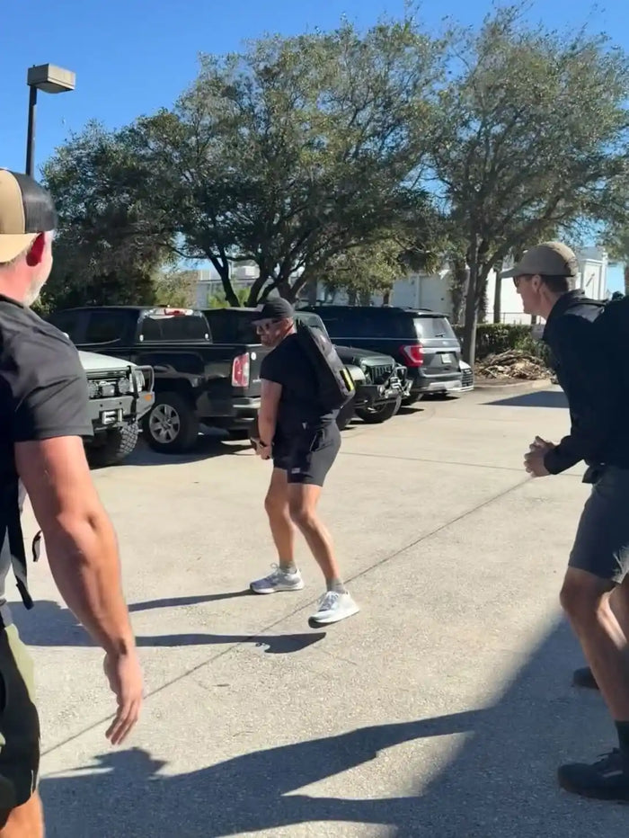 Three people wearing GORUCK gear and backpacks outside in a parking lot, preparing for a rucking workout.