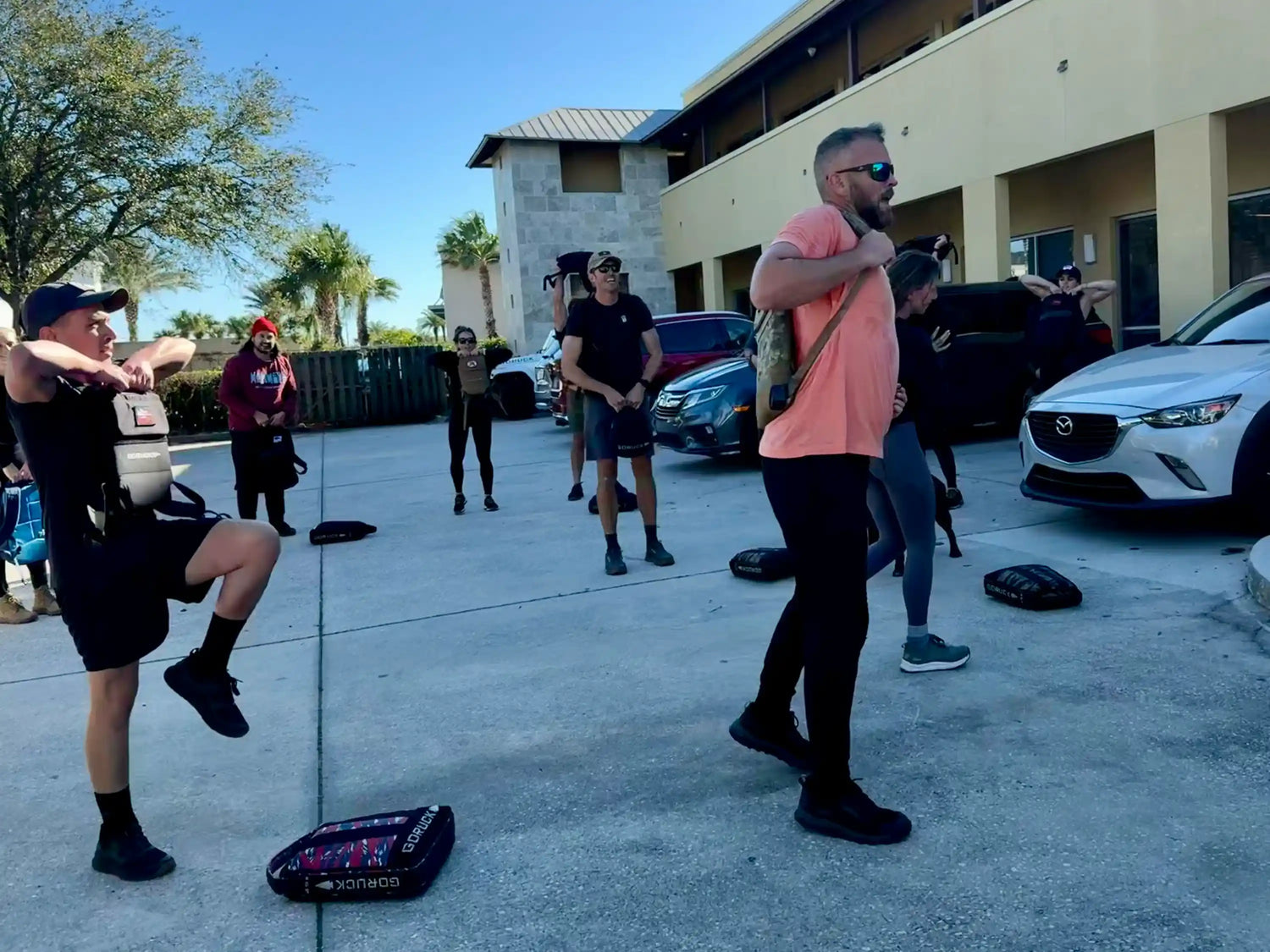 Group outdoor rucking workout with GORUCK gear, participants lifting weighted backpacks