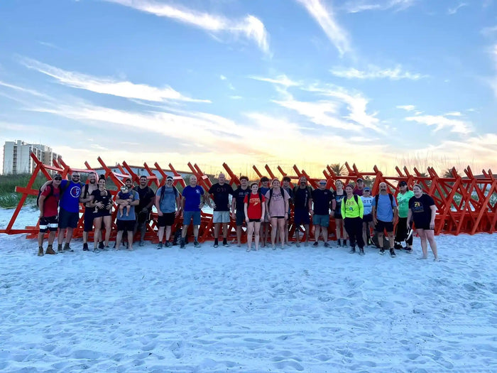 GORUCK group on beach with rucking gear in front of orange obstacle at sunset