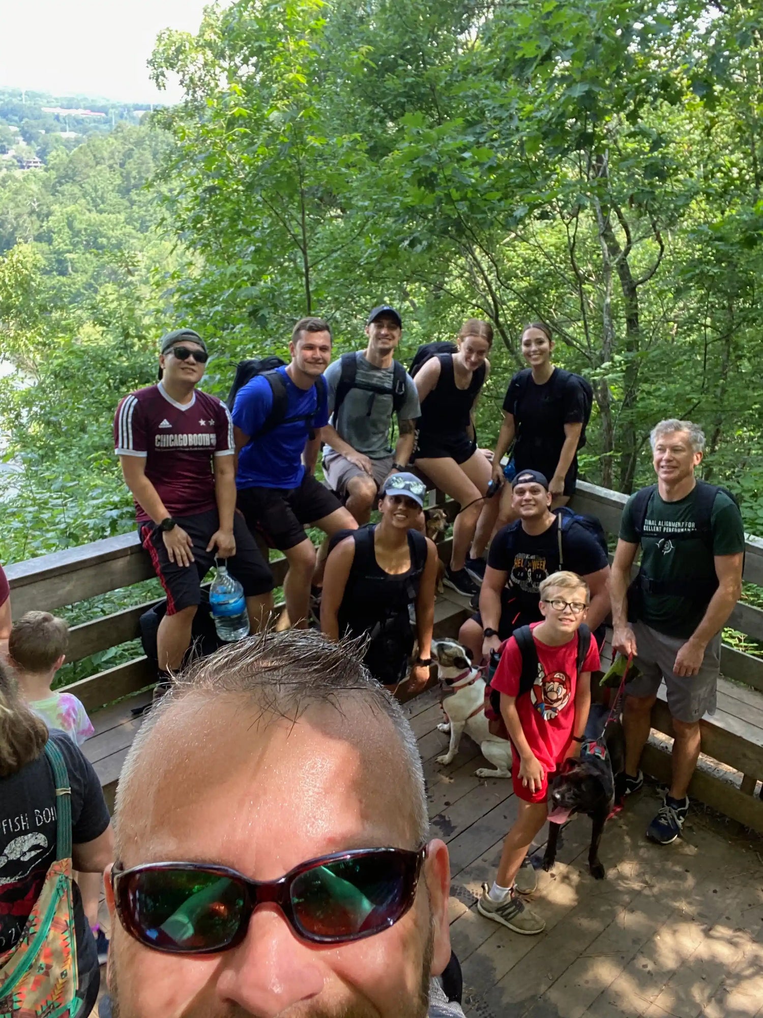 GORUCK rucking group outdoors on a wooden deck, wearing backpacks, with dogs and lush forest view