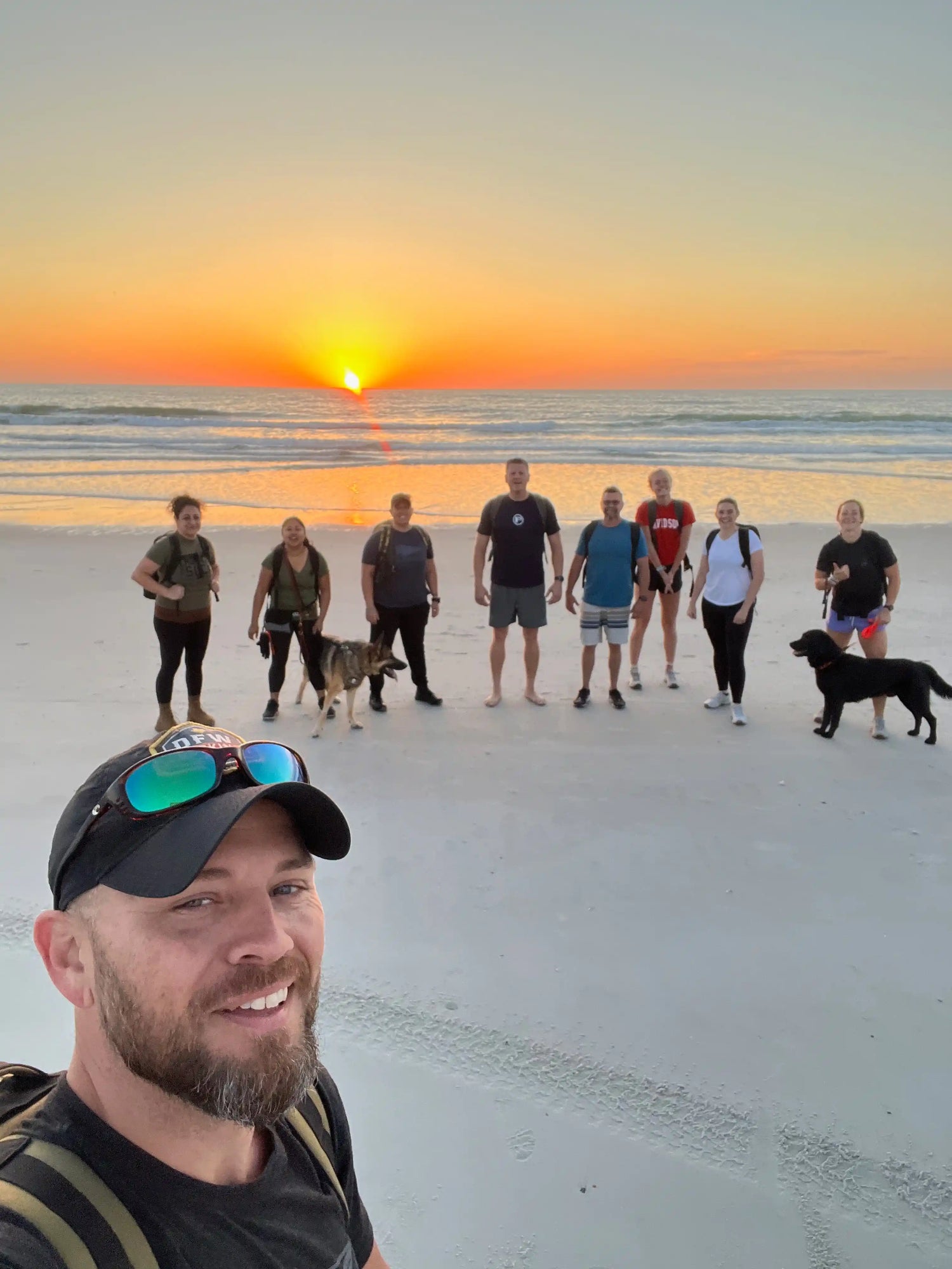 GORUCK rucking group with backpacks and dogs on beach at sunrise, team fitness activity