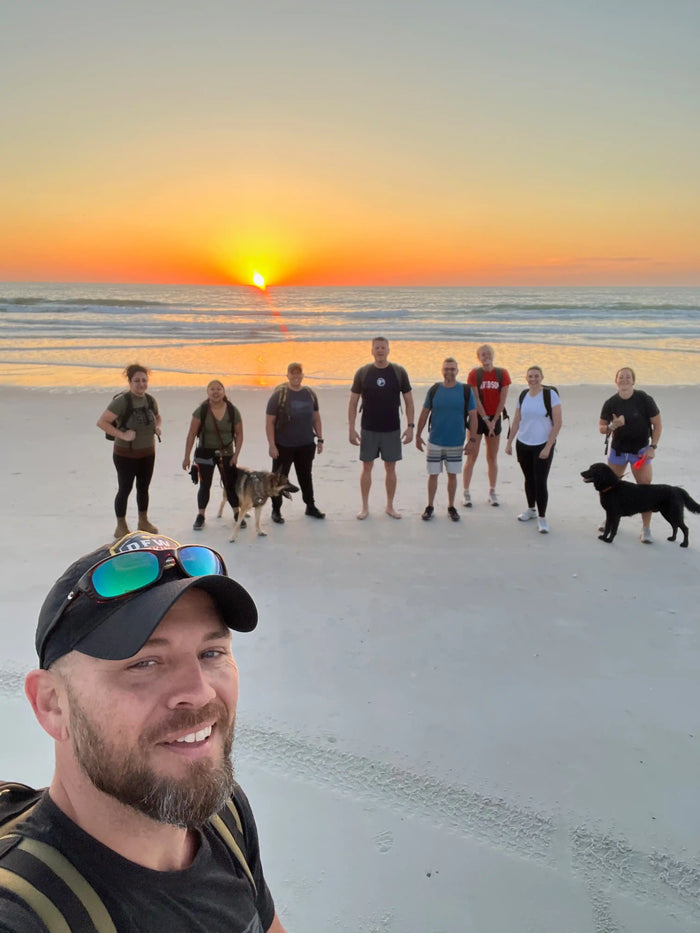 GORUCK rucking group with backpacks and dogs on beach at sunrise, team fitness activity