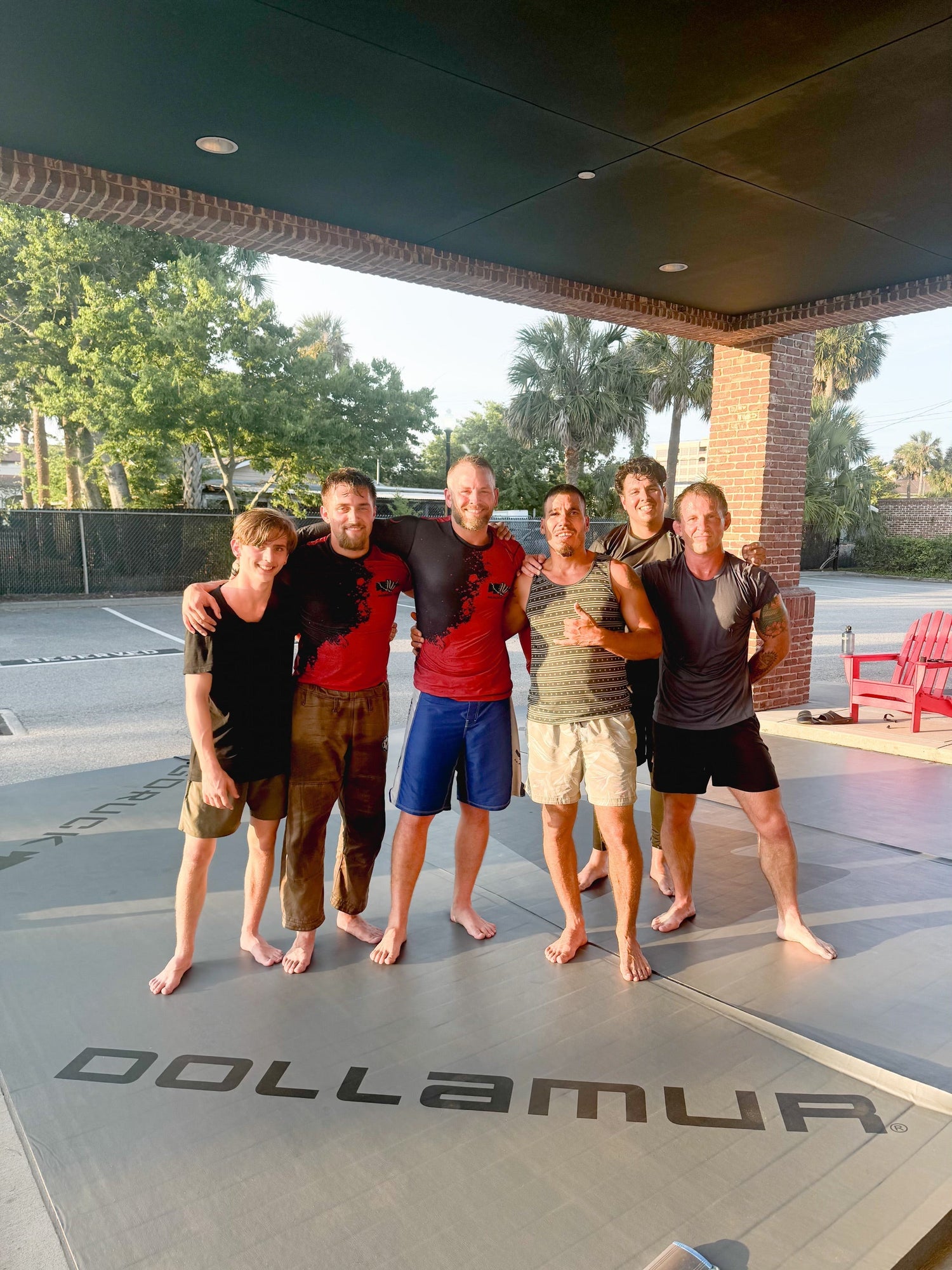 Group of men in athletic gear posing on outdoor GORUCK training mat under covered area