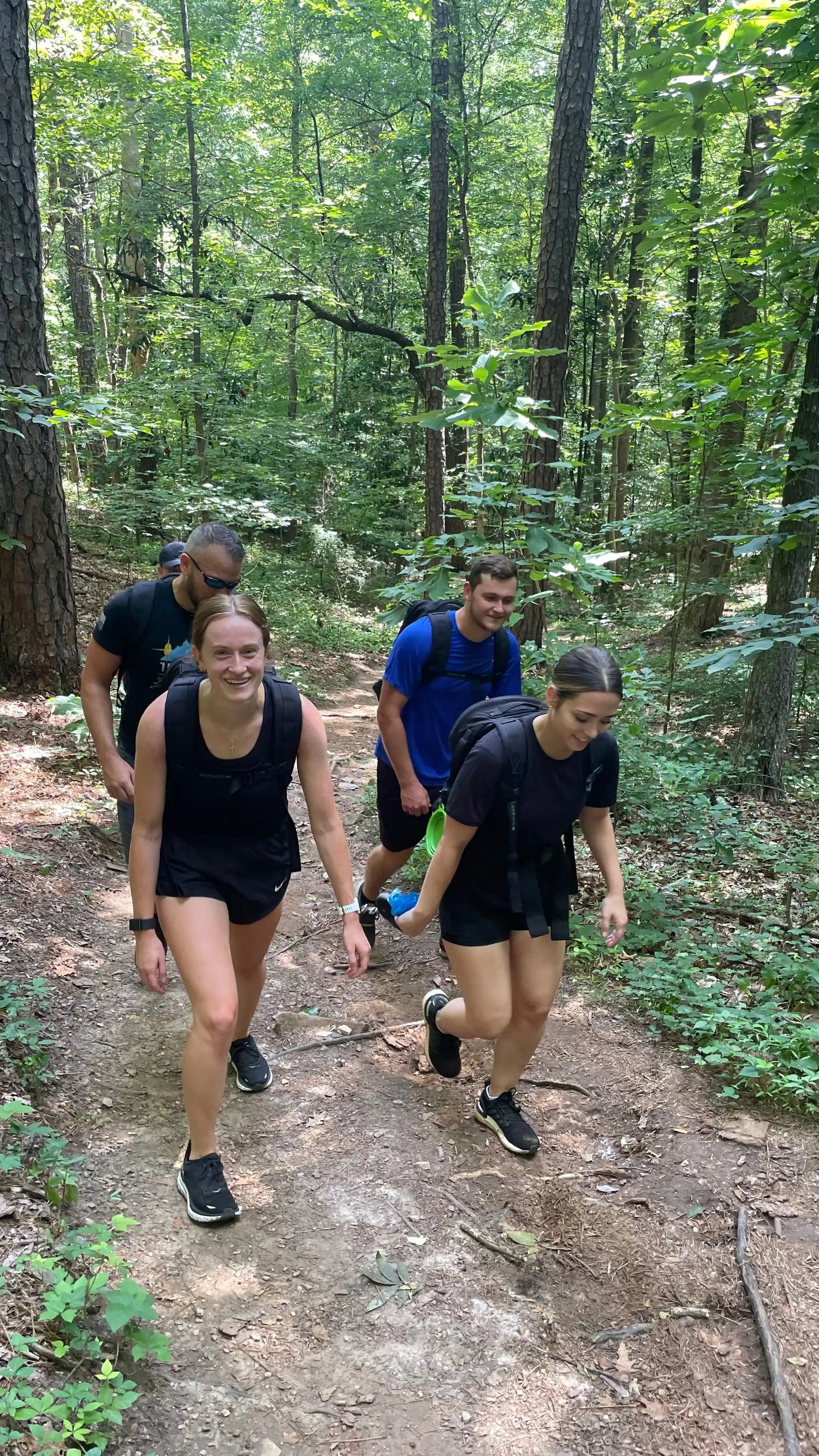 Group wearing GORUCK rucksacks hiking on a wooded forest trail, outdoor adventure gear