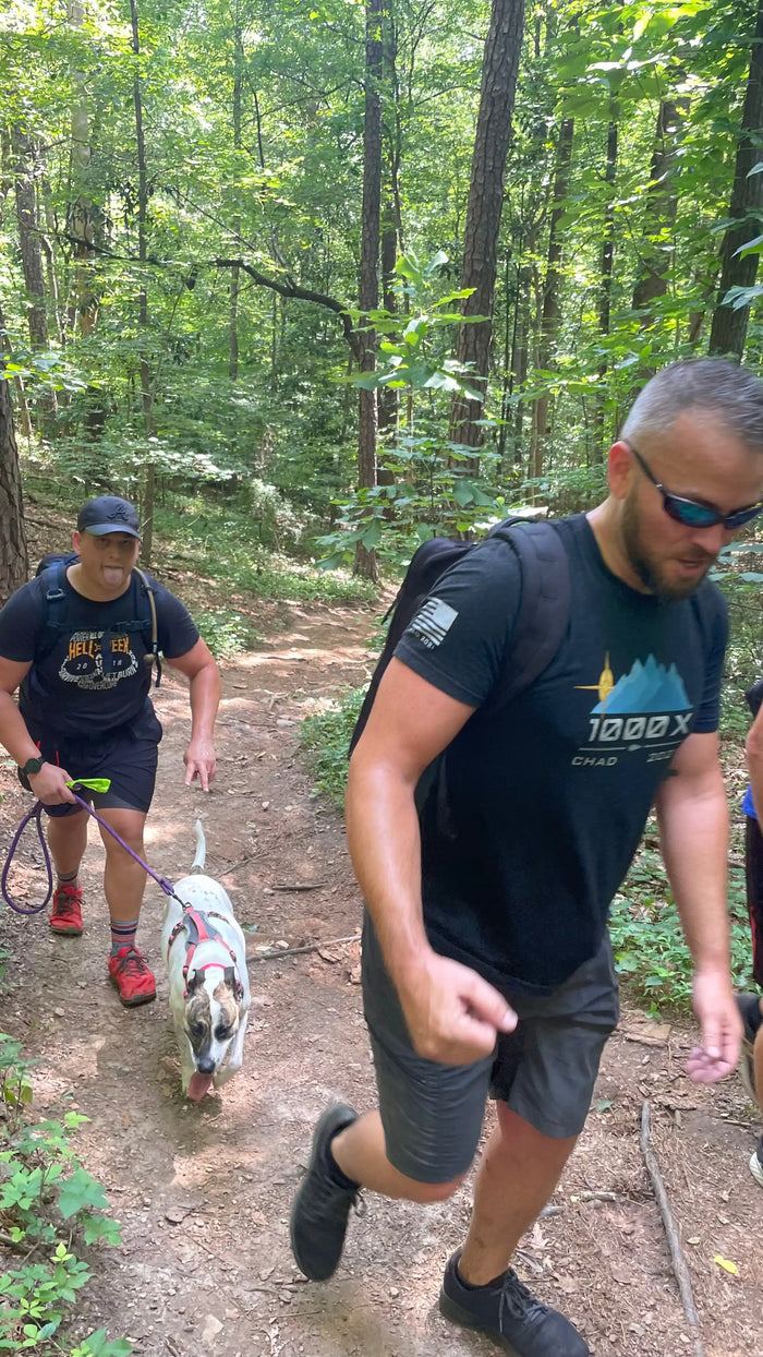 Two men rucking with backpacks and a dog on a wooded trail wearing GORUCK gear