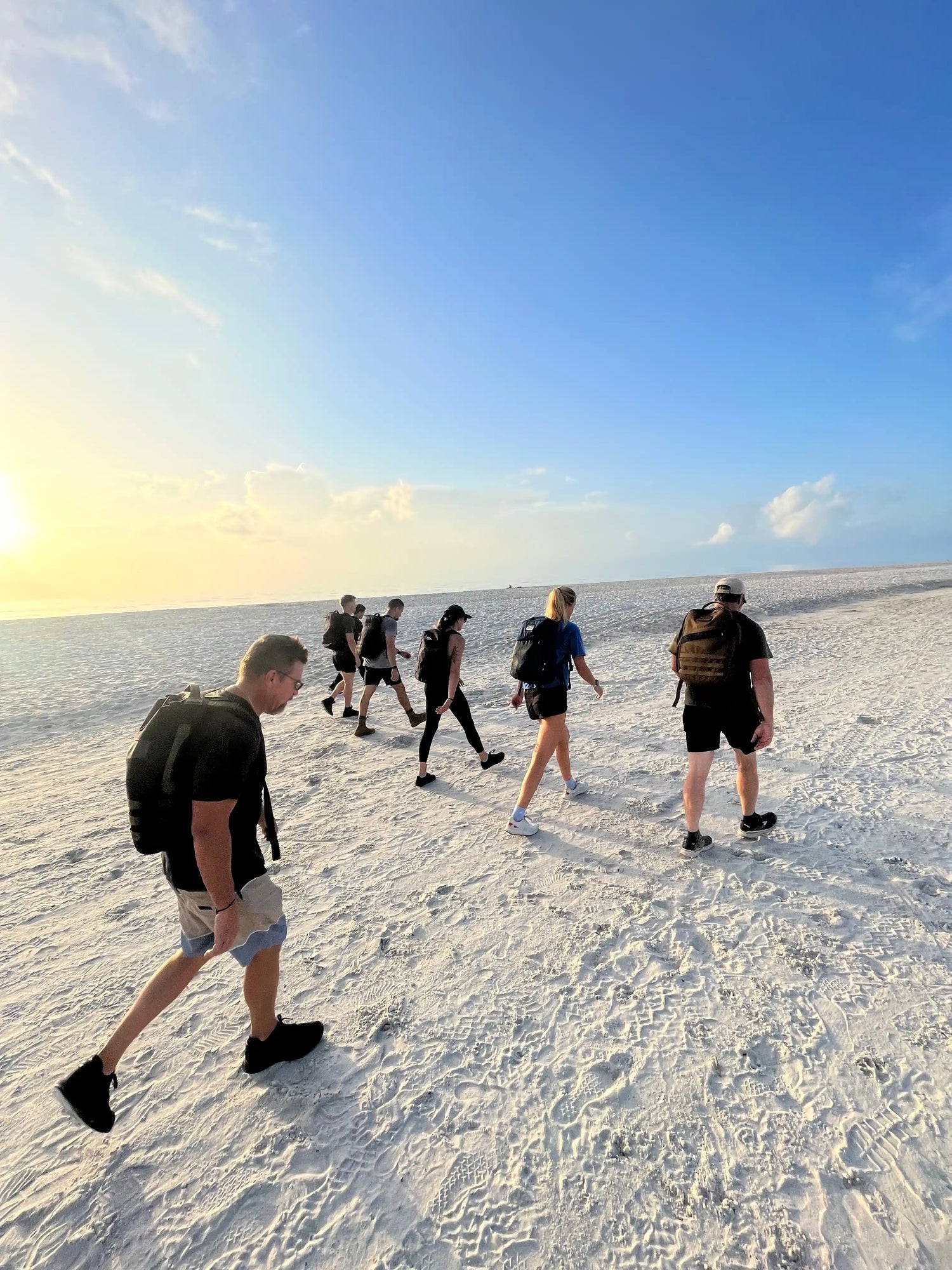 Group of people rucking with GORUCK backpacks on a sandy beach at sunrise