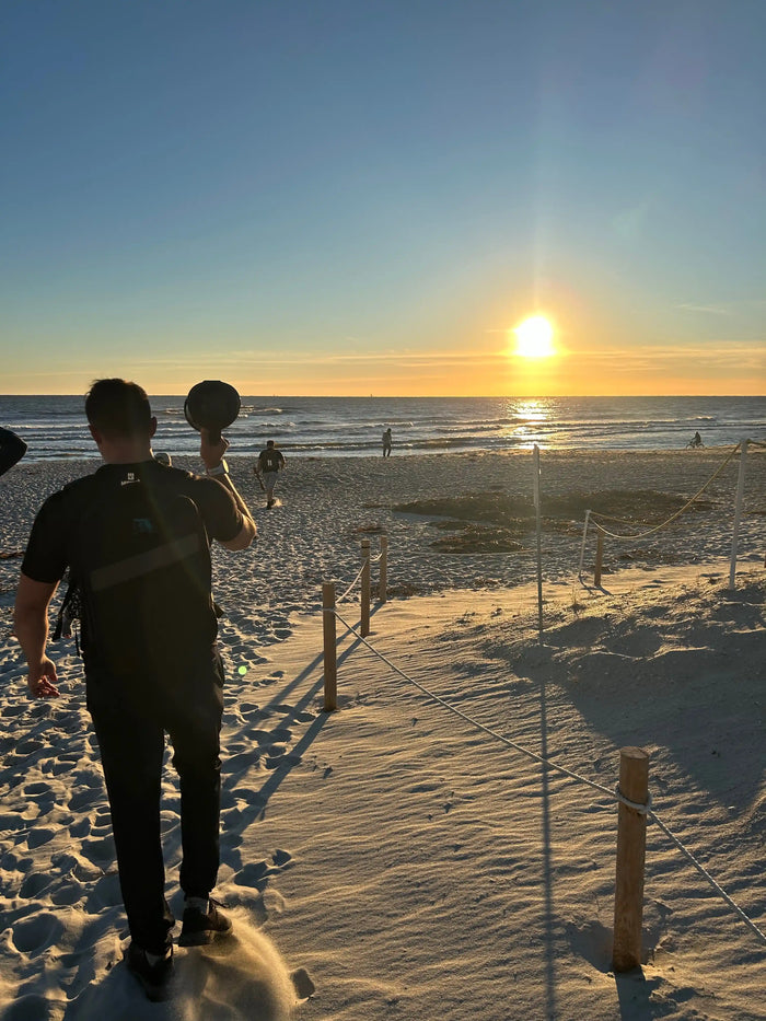 GORUCK athlete carrying weight on sandy beach at sunset during rucking event