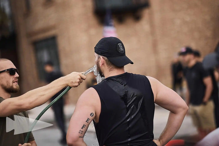 GORUCK participant cooling off with hose during outdoor rucking event, community fitness