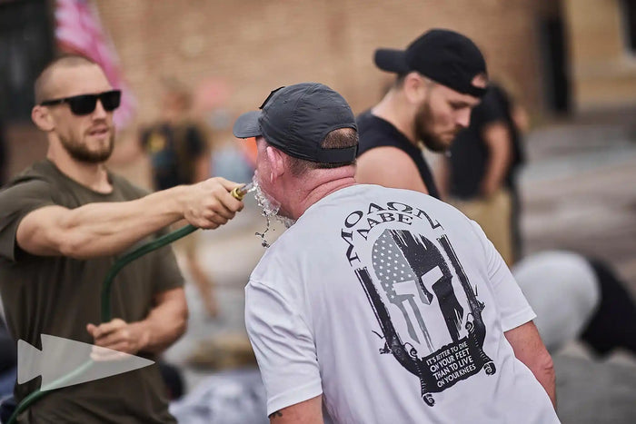 GORUCK participants during outdoor rucking event, man rinsing face with water hose, teamwork focus