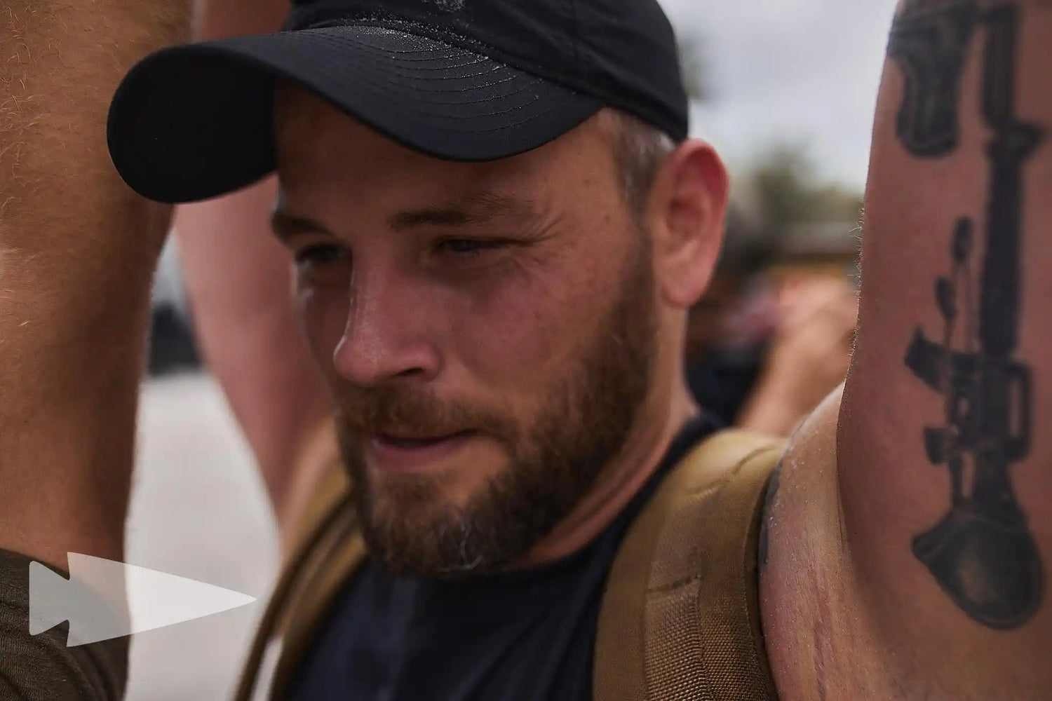 Man wearing black cap and rucksack training outdoors at GORUCK rucking event, close-up view.
