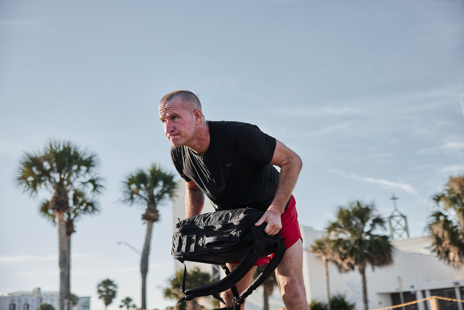 Man rucking outdoors with GORUCK backpack, sunny day, palm trees in the background