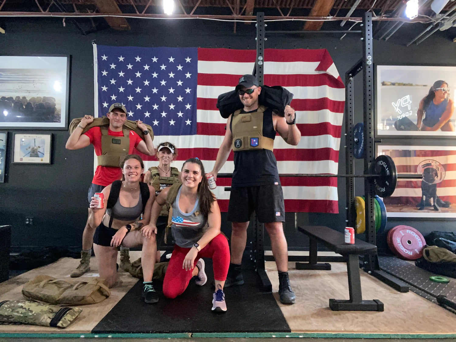 Group wearing GORUCK gear posing in gym with American flag, rucking equipment visible