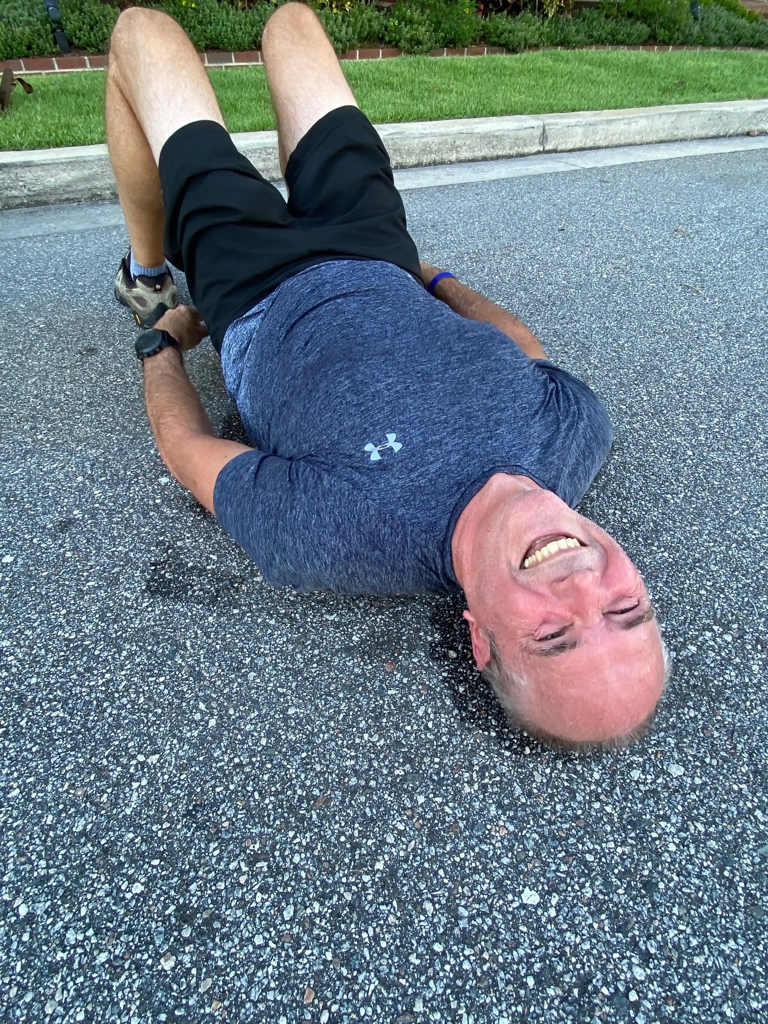 Man in athletic gear smiling while exercising on pavement, showcasing GORUCK rucking activity