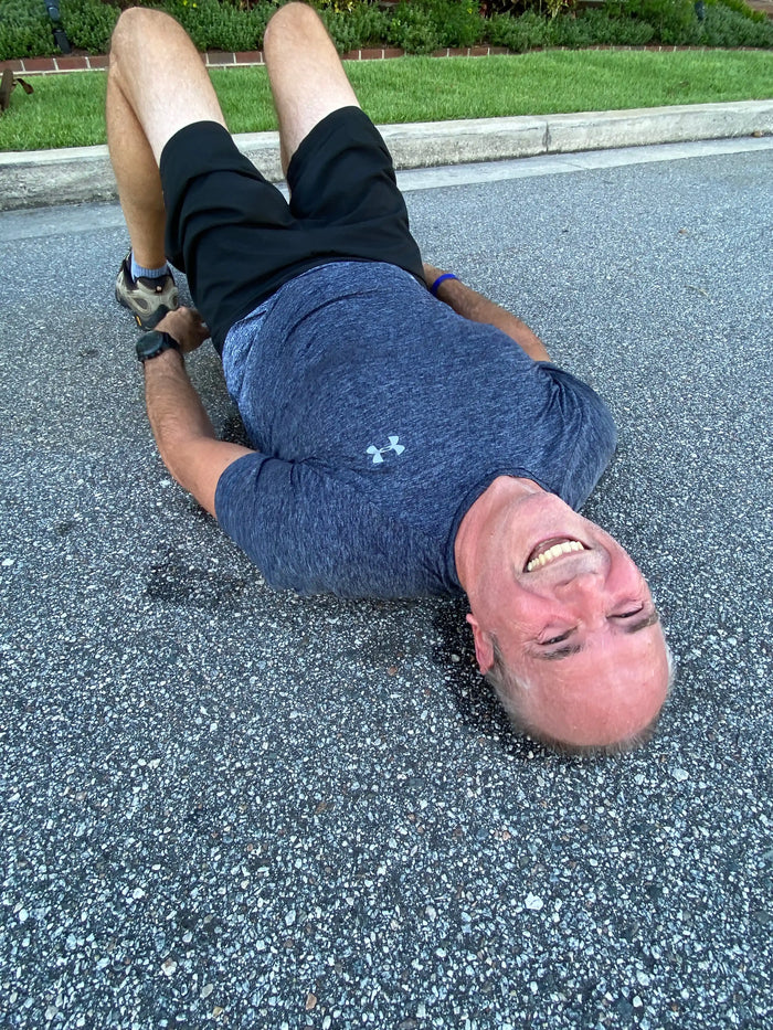 Man in workout clothes smiling while exercising outdoors on pavement, GORUCK fitness training