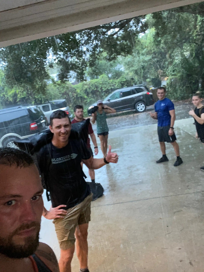 GORUCK team rucking in heavy rain, wearing athletic gear, standing by parked cars