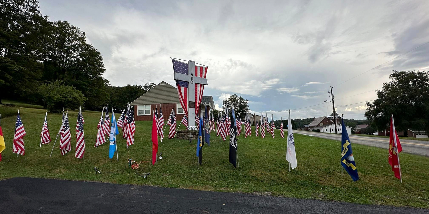 Outdoor 9/11 memorial with American flags, cross, and GORUCK tribute on a grassy lawn