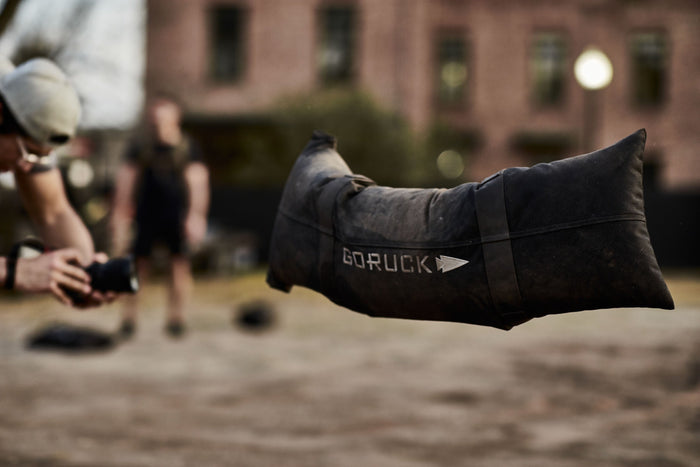 GORUCK sandbag midair during outdoor rucking workout, focus on rugged training gear