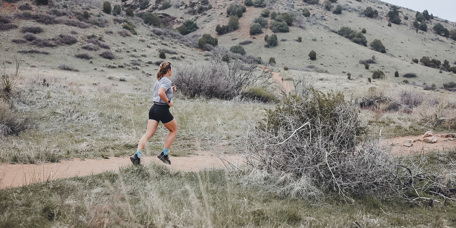 Woman trail running on a dirt path in rugged outdoor landscape wearing GORUCK gear