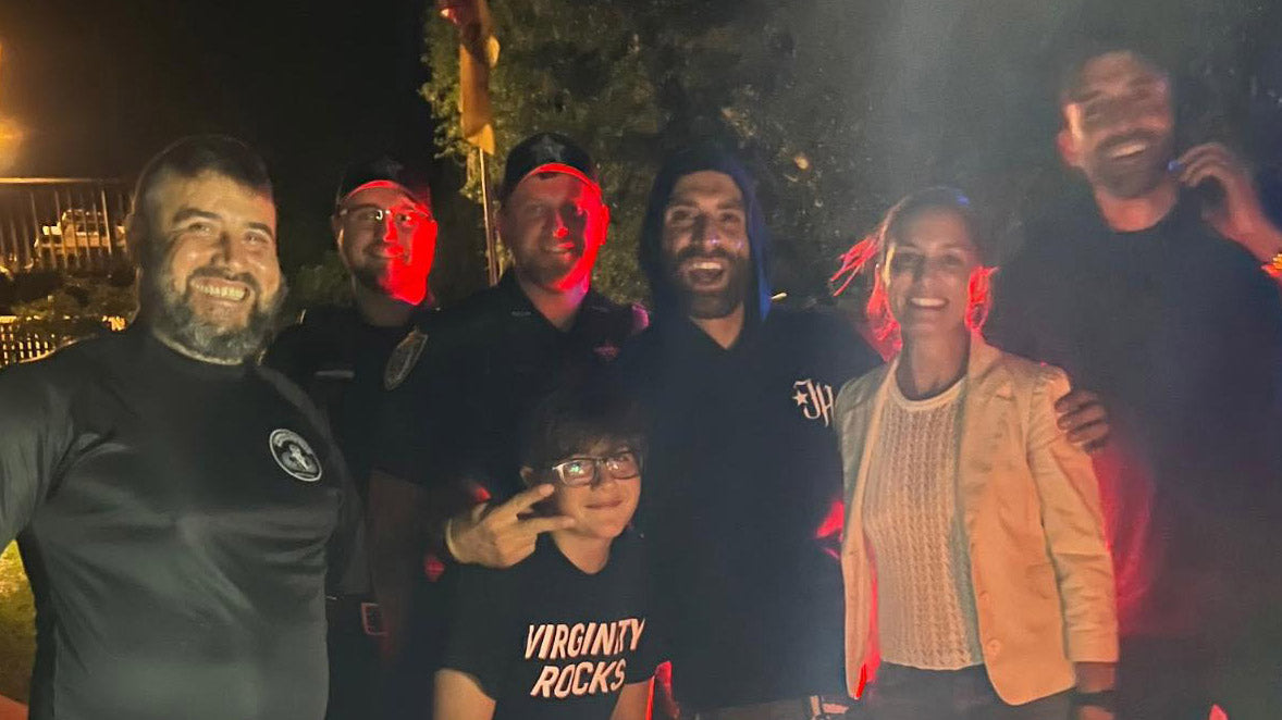 Group of people smiling outdoors at night with two uniformed officers, illuminated by red lights