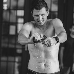 A shirtless man wrings out wet fabric, water dripping down his torso in a black-and-white shot—capturing the tough spirit behind the Embrace the Suck Tee - Tri-BlendX.