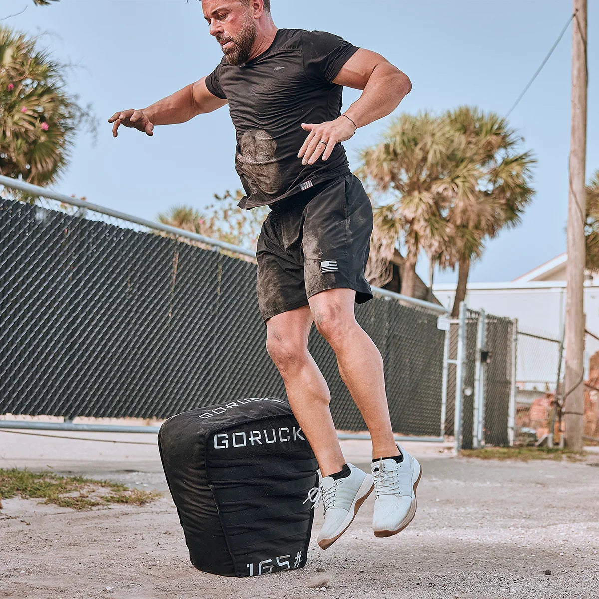 Man jumping onto GORUCK sandbag outdoors, showcasing durable rucking gear in action
