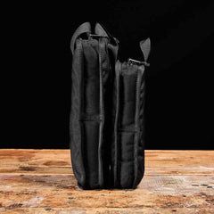 Two black GORUCK rucking pouches standing upright on a wooden surface against a black background