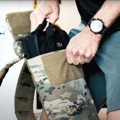 Person loading a 15lb GORUCK sand plate into a camouflage ruck backpack
