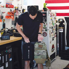 Man holding GORUCK 15lb sand plate and ruck in garage gym with American flag background