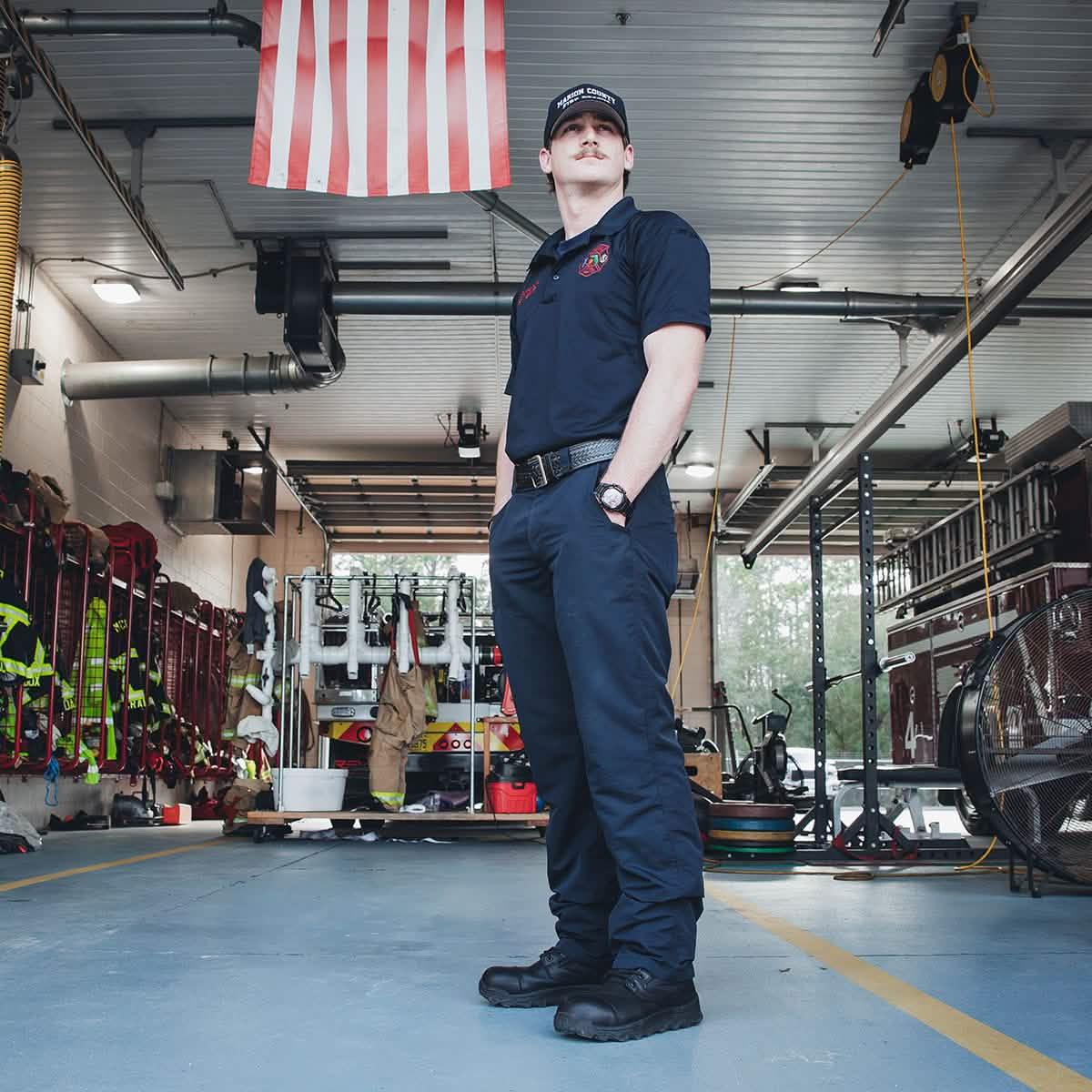 Firefighter in navy GORUCK pants stands in fire station under American flag