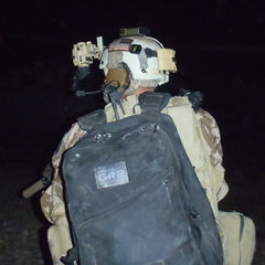 At night, a soldier wearing a helmet and large GR2 - Cordura backpack walks away, with gear attached to both helmet and uniform.