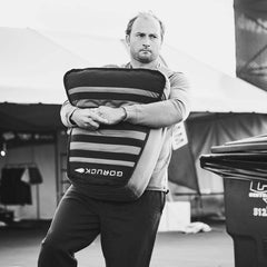Man holding GORUCK rucking sandbag outdoors at fitness event tent
