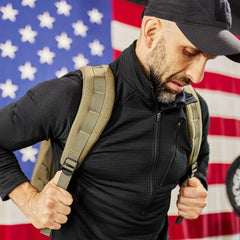 Man wearing GORUCK rucking backpack and black jacket in front of American flag
