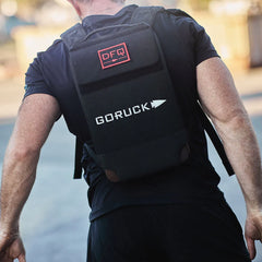 Man wearing GORUCK rucking backpack outdoors, featuring DFQ patch and tough gear design
