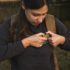 Woman securing a tan GORUCK rucksack outdoors, showcasing durable rucking gear