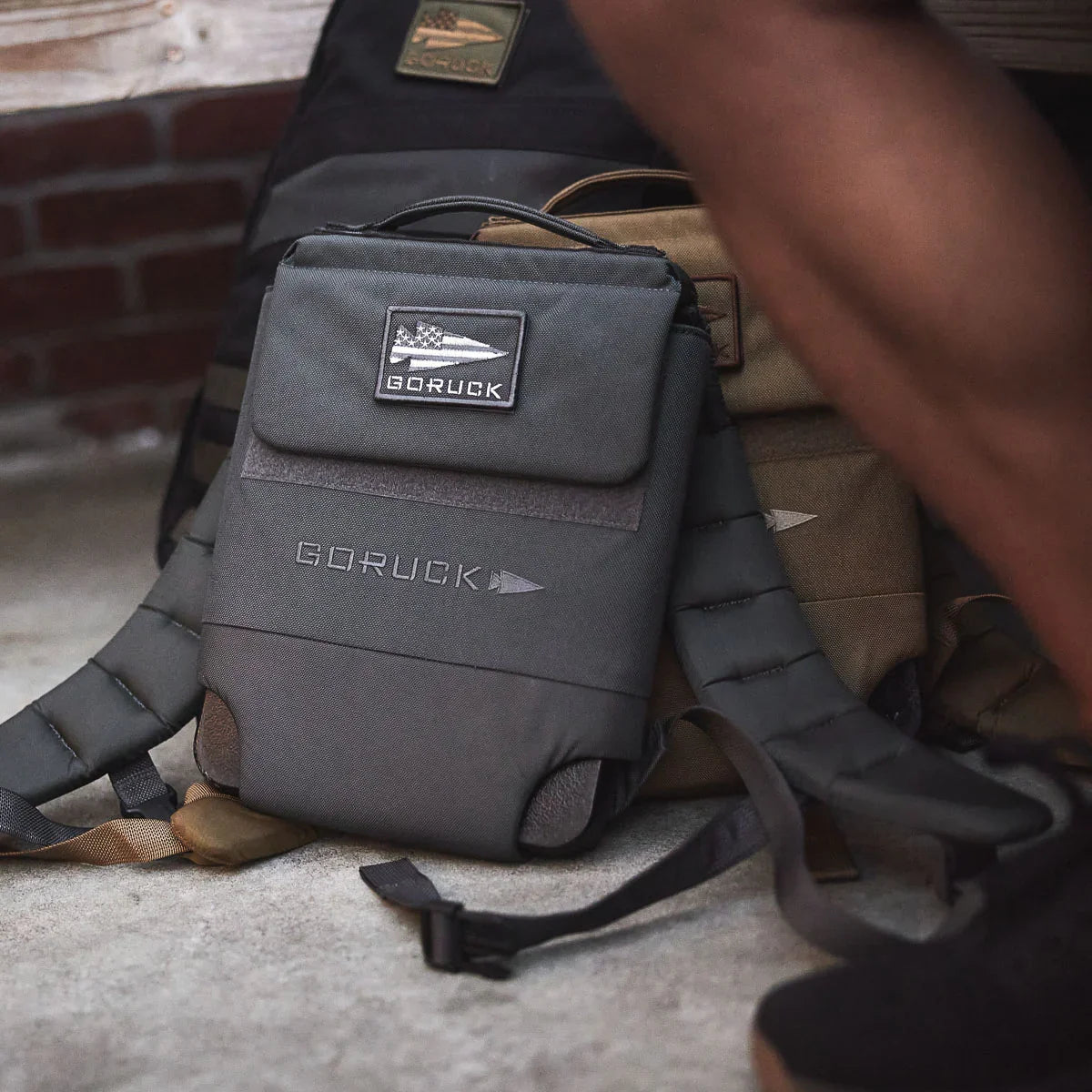 GORUCK rucking backpack on concrete near brick wall, showcasing rugged design and logo patch