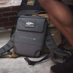 GORUCK rucking backpack on concrete near brick wall, showcasing rugged design and logo patch