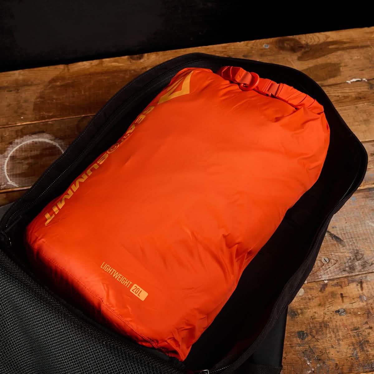Bright orange 20L lightweight packing bag inside an open GORUCK rucksack on wooden table
