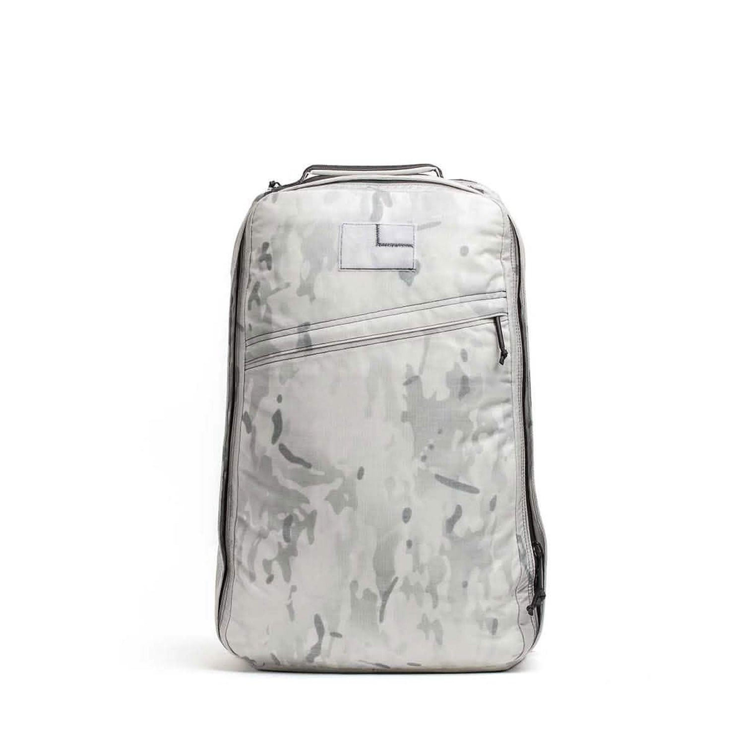 The GR1 is a light gray camo-patterned rucksack with a top handle and diagonal front zipper pocket, inspired by the iconic Special Forces backpack, displayed on a white background.