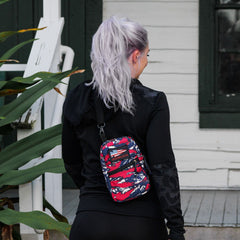 A woman with long, silver hair stands outside a white house, wearing the GRenade Ruck - American Tiger Stripe cross-body bag.